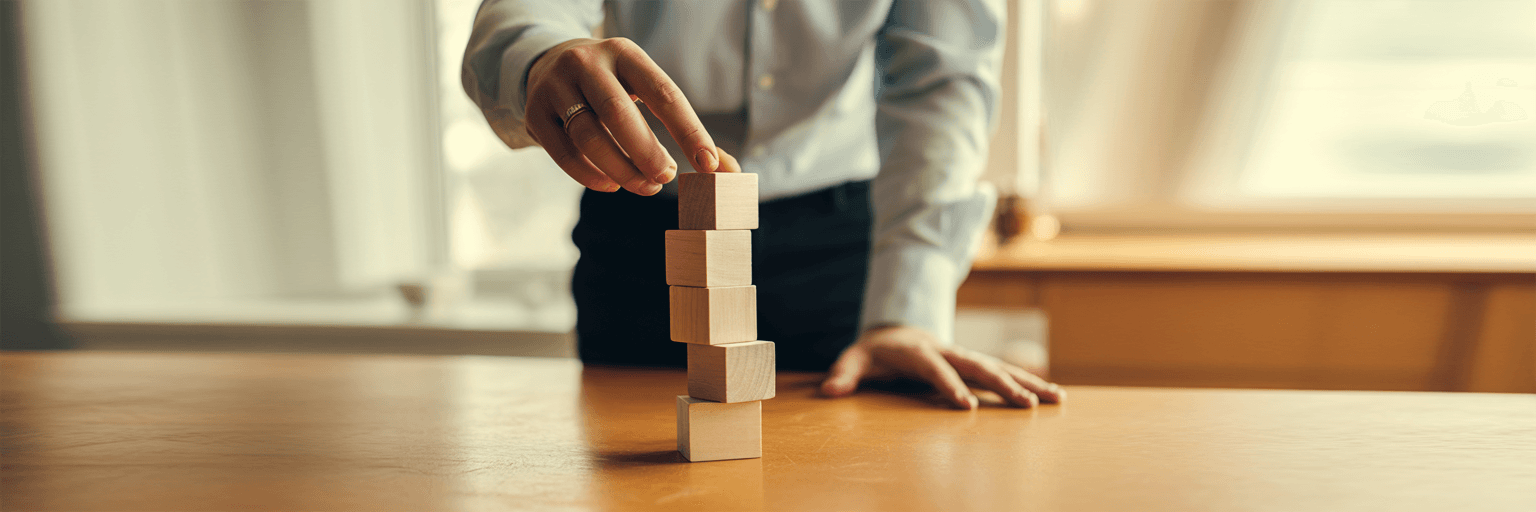 Hands stacking small blank wooden blocks of varying heights into a neat tower.