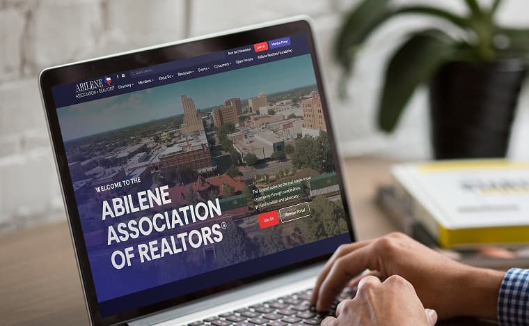 Laptop showing the Abilene Association of REALTORS® homepage over an aerial view of downtown Abilene